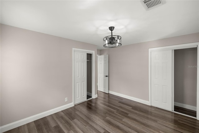 unfurnished bedroom with an inviting chandelier and dark hardwood / wood-style flooring