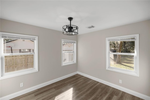 spare room featuring an inviting chandelier and dark wood-type flooring