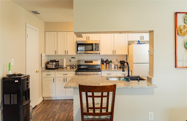 kitchen featuring a breakfast bar, sink, light stone counters, white cabinets, and appliances with stainless steel finishes