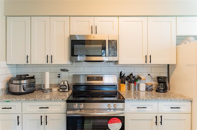 kitchen with stainless steel appliances, light stone countertops, backsplash, and white cabinets