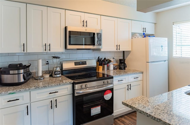 kitchen with hardwood / wood-style floors, light stone counters, backsplash, appliances with stainless steel finishes, and white cabinetry