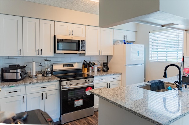 kitchen with dark wood-type flooring, light stone countertops, appliances with stainless steel finishes, and white cabinetry