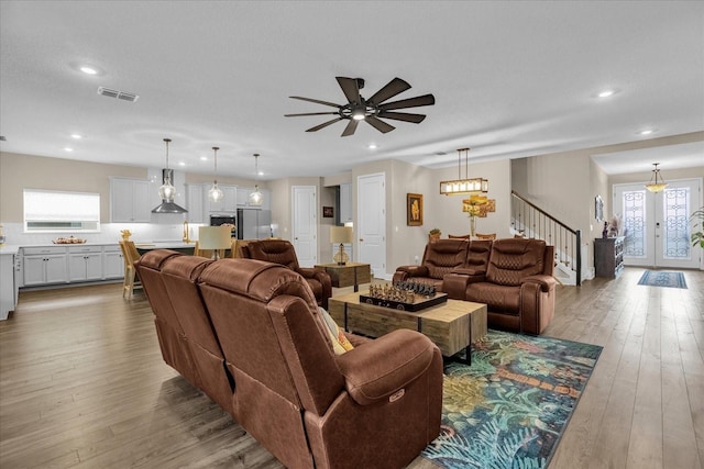 living room with french doors, ceiling fan with notable chandelier, light hardwood / wood-style flooring, and a wealth of natural light