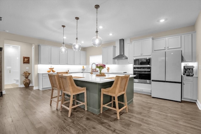 kitchen featuring wall chimney range hood, white cabinetry, stainless steel appliances, a breakfast bar, and hardwood / wood-style floors