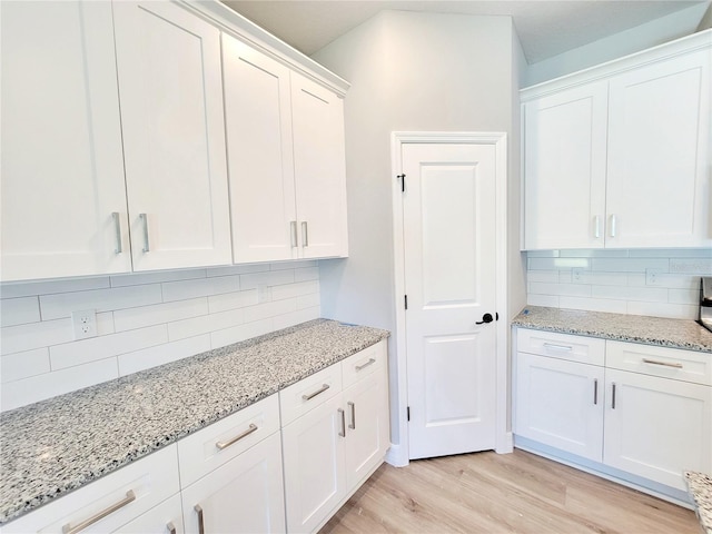 kitchen featuring white cabinetry, light stone counters, decorative backsplash, and light hardwood / wood-style flooring