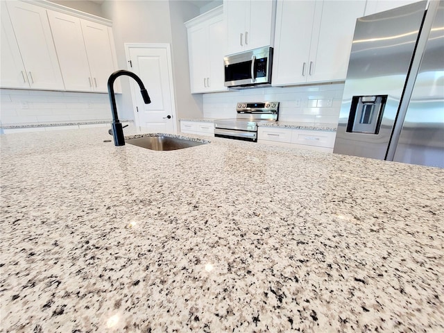 kitchen featuring white cabinets, stainless steel appliances, sink, and light stone counters