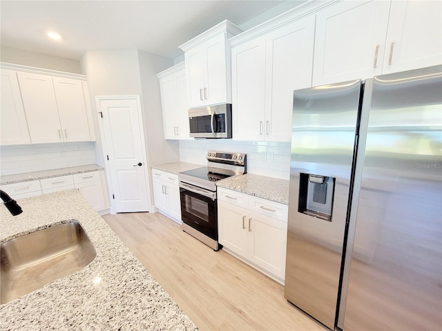 kitchen with white cabinets, stainless steel appliances, light wood-type flooring, and backsplash