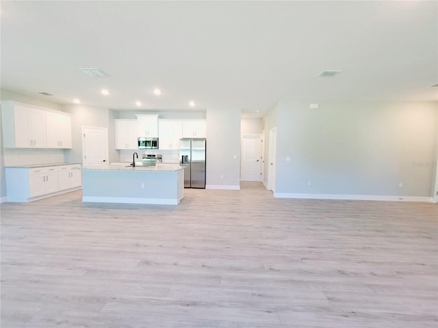 kitchen with an island with sink, stainless steel appliances, light hardwood / wood-style floors, and white cabinetry