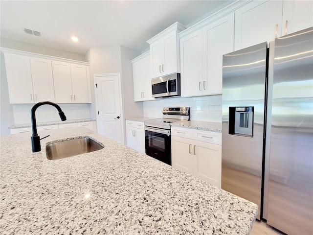 kitchen with appliances with stainless steel finishes, sink, decorative backsplash, and white cabinets