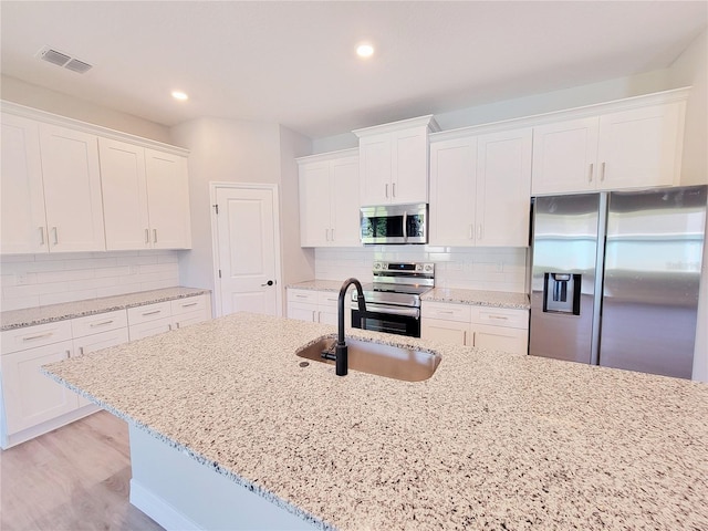 kitchen featuring decorative backsplash, stainless steel appliances, sink, light stone countertops, and white cabinetry