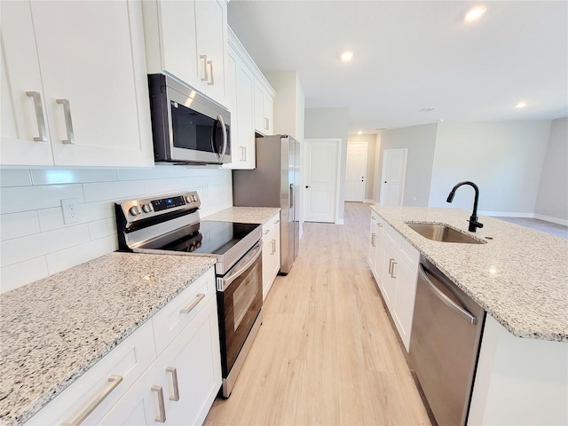 kitchen with sink, white cabinetry, light hardwood / wood-style floors, stainless steel appliances, and a kitchen island with sink