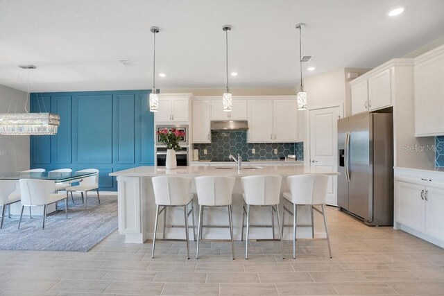 kitchen with appliances with stainless steel finishes, pendant lighting, sink, and an island with sink