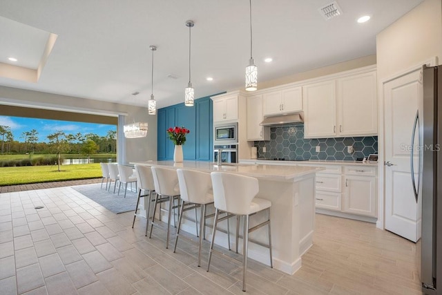 kitchen featuring white cabinets, pendant lighting, a kitchen island with sink, backsplash, and stainless steel appliances