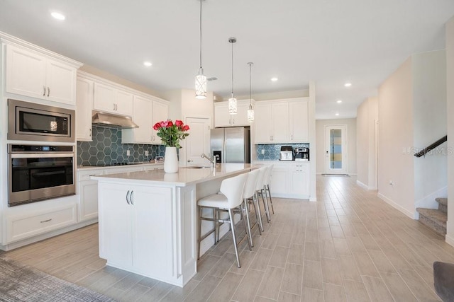 kitchen with an island with sink, white cabinetry, stainless steel appliances, and tasteful backsplash