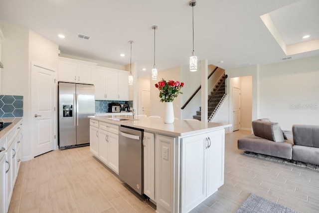 kitchen with decorative light fixtures, a center island with sink, white cabinetry, appliances with stainless steel finishes, and decorative backsplash