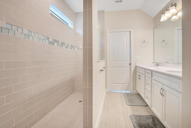 bathroom with a tile shower, vanity, and vaulted ceiling