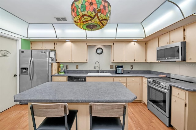 kitchen featuring backsplash, appliances with stainless steel finishes, cream cabinetry, light hardwood / wood-style floors, and sink