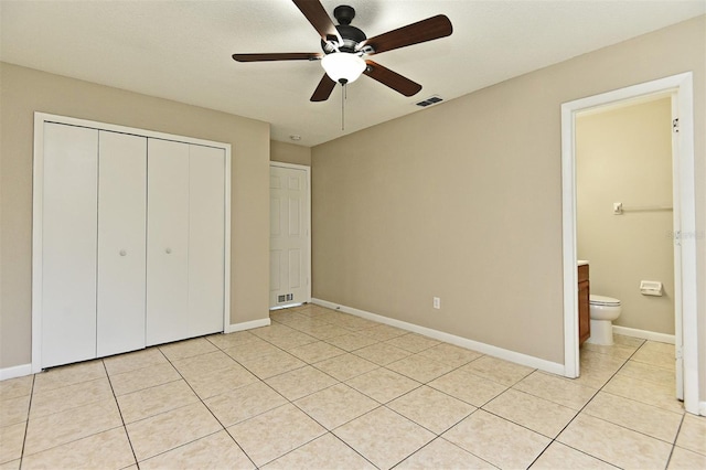 unfurnished bedroom featuring ceiling fan, light tile patterned floors, a textured ceiling, a closet, and ensuite bathroom