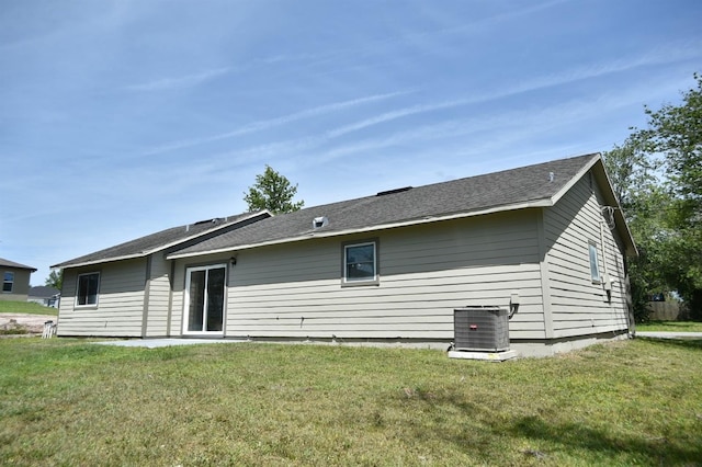 rear view of house with central air condition unit and a lawn