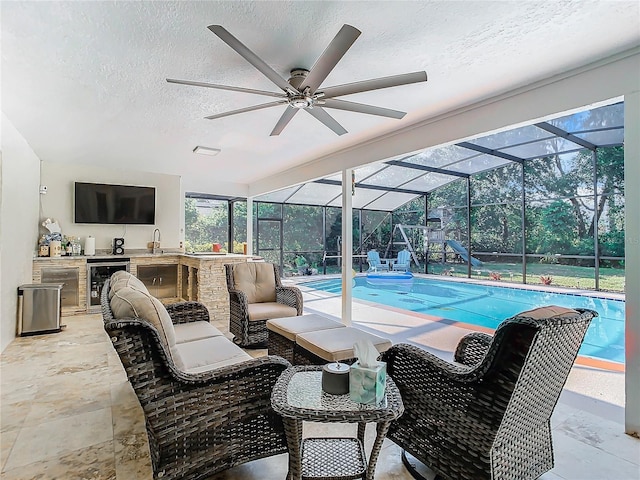 view of pool with exterior kitchen, a patio, glass enclosure, and ceiling fan