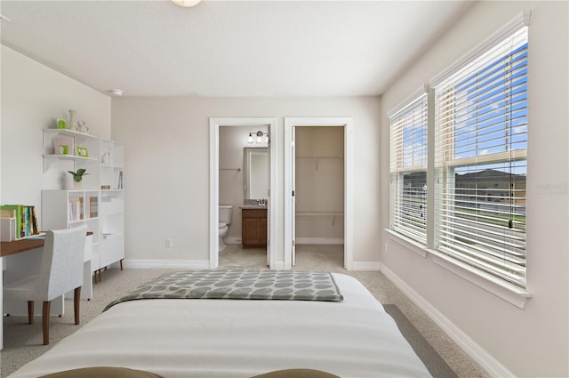 bedroom featuring a spacious closet, light colored carpet, a closet, and ensuite bath