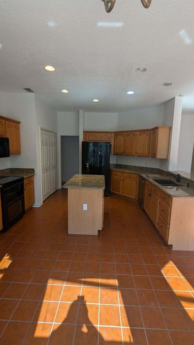 kitchen featuring a textured ceiling, black appliances, sink, a center island, and tile patterned floors