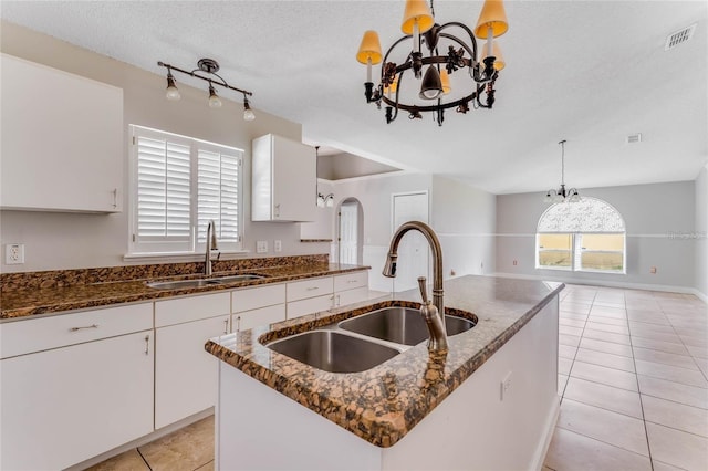 kitchen with sink, a textured ceiling, decorative light fixtures, a kitchen island with sink, and an inviting chandelier