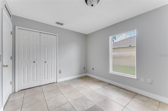 unfurnished bedroom with a textured ceiling, a closet, multiple windows, and light tile patterned flooring