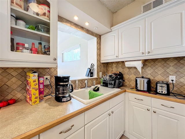 kitchen with tasteful backsplash, white cabinetry, and sink