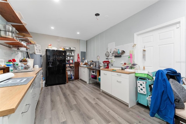 kitchen featuring wooden counters, black fridge, light wood-type flooring, and white cabinetry