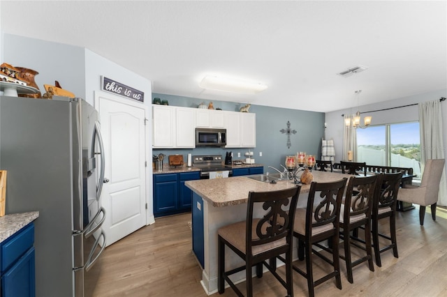 kitchen with blue cabinets, hanging light fixtures, appliances with stainless steel finishes, a kitchen breakfast bar, and light wood-type flooring