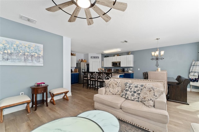 living room featuring ceiling fan with notable chandelier and light hardwood / wood-style floors