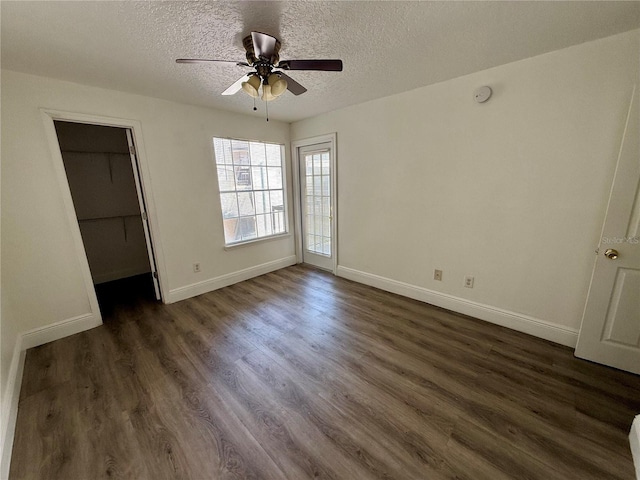 unfurnished bedroom with ceiling fan, a textured ceiling, a walk in closet, and dark hardwood / wood-style floors