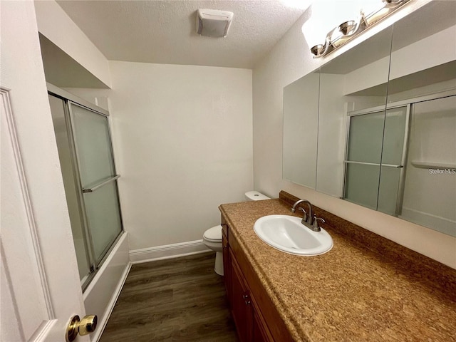 full bathroom featuring toilet, hardwood / wood-style floors, vanity, combined bath / shower with glass door, and a textured ceiling