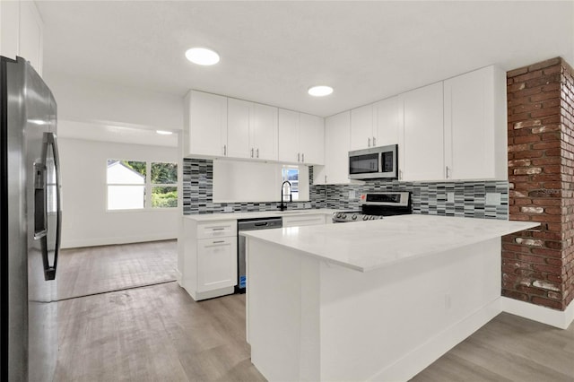 kitchen with light stone countertops, stainless steel appliances, white cabinets, light hardwood / wood-style flooring, and backsplash