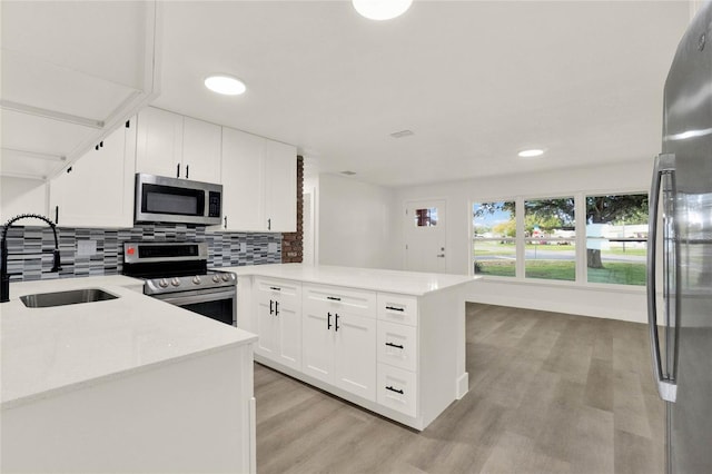 kitchen featuring sink, kitchen peninsula, white cabinetry, light hardwood / wood-style flooring, and appliances with stainless steel finishes