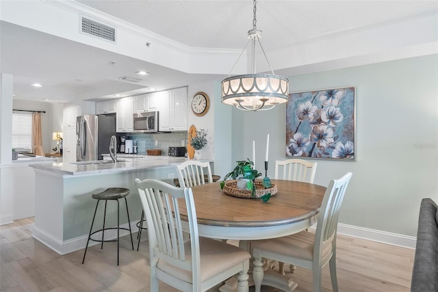 dining room featuring ornamental molding, sink, and light hardwood / wood-style flooring