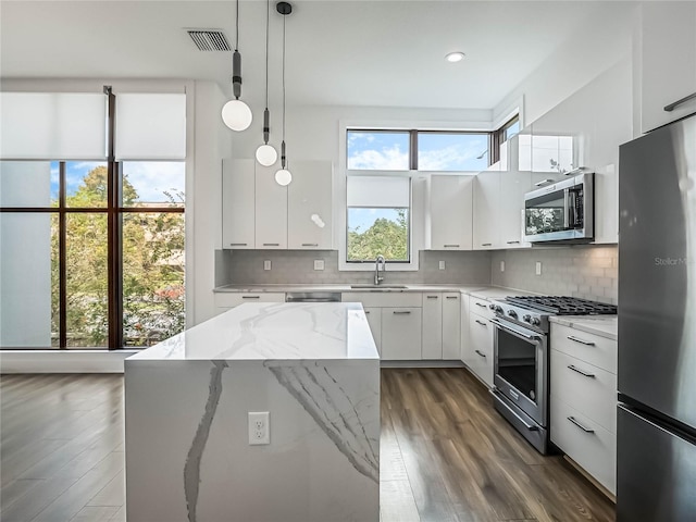 kitchen featuring a kitchen island, decorative light fixtures, sink, stainless steel appliances, and white cabinets