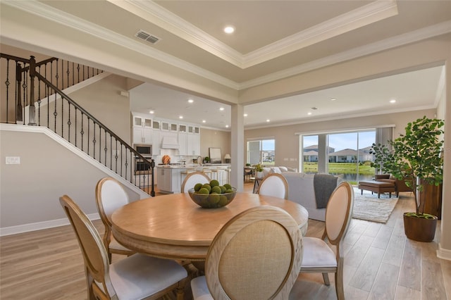 dining space with ornamental molding, a tray ceiling, and light hardwood / wood-style floors