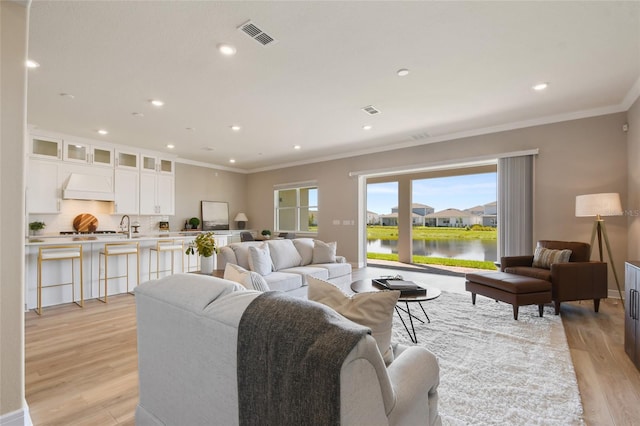 living room featuring light hardwood / wood-style floors, crown molding, and a water view