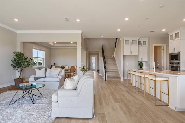 living room featuring ornamental molding, sink, and light wood-type flooring