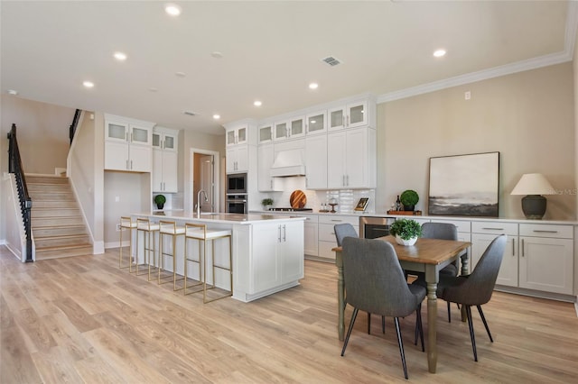 kitchen with appliances with stainless steel finishes, a kitchen island with sink, light hardwood / wood-style flooring, and white cabinets