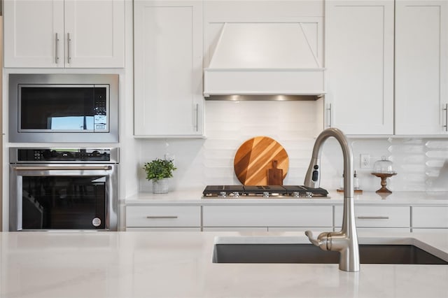 kitchen featuring custom exhaust hood, white cabinets, backsplash, sink, and stainless steel appliances