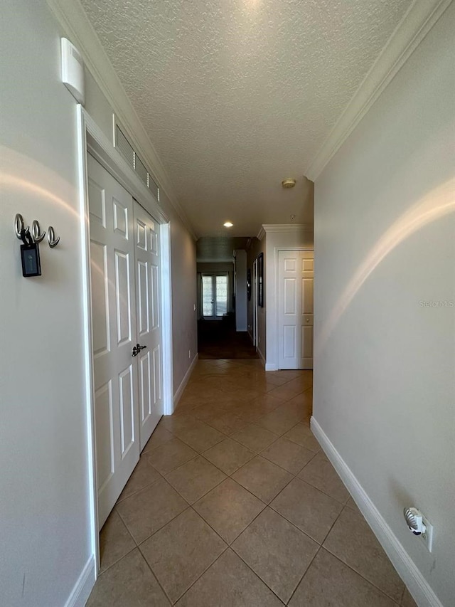 corridor featuring crown molding, a textured ceiling, and light tile patterned floors