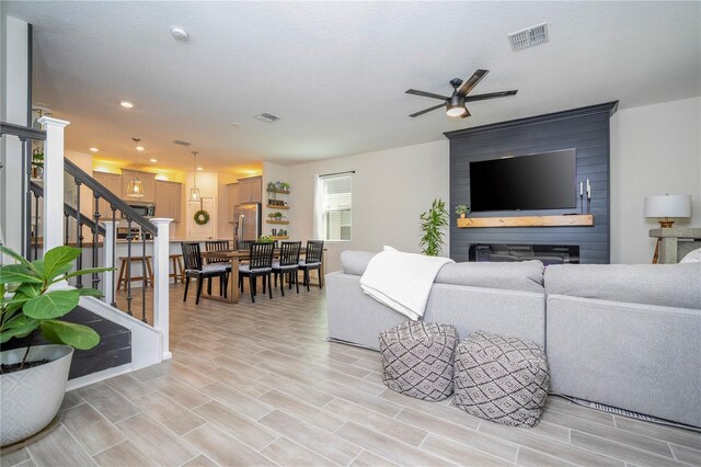 living room featuring a fireplace, light hardwood / wood-style flooring, a textured ceiling, and ceiling fan