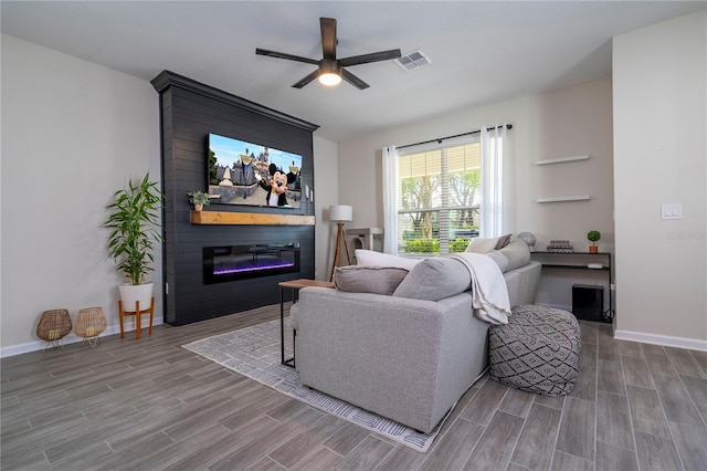 living room with hardwood / wood-style flooring, ceiling fan, and a large fireplace