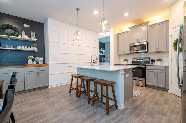 kitchen with stainless steel appliances, a breakfast bar, gray cabinetry, light hardwood / wood-style flooring, and decorative light fixtures