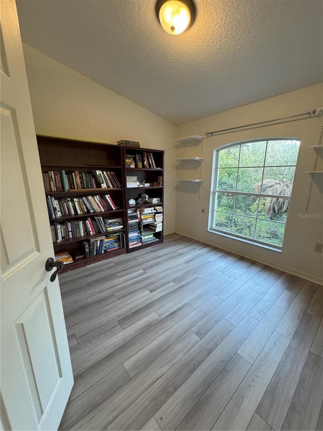 spare room with a textured ceiling, light wood-type flooring, and vaulted ceiling