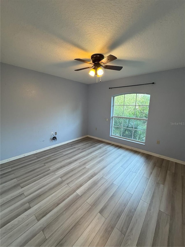 spare room with baseboards, a ceiling fan, wood finished floors, and a textured ceiling