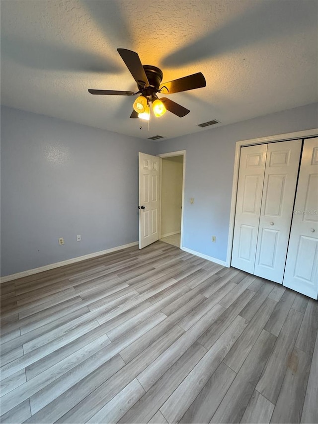 unfurnished bedroom featuring a textured ceiling, baseboards, visible vents, wood finished floors, and a closet